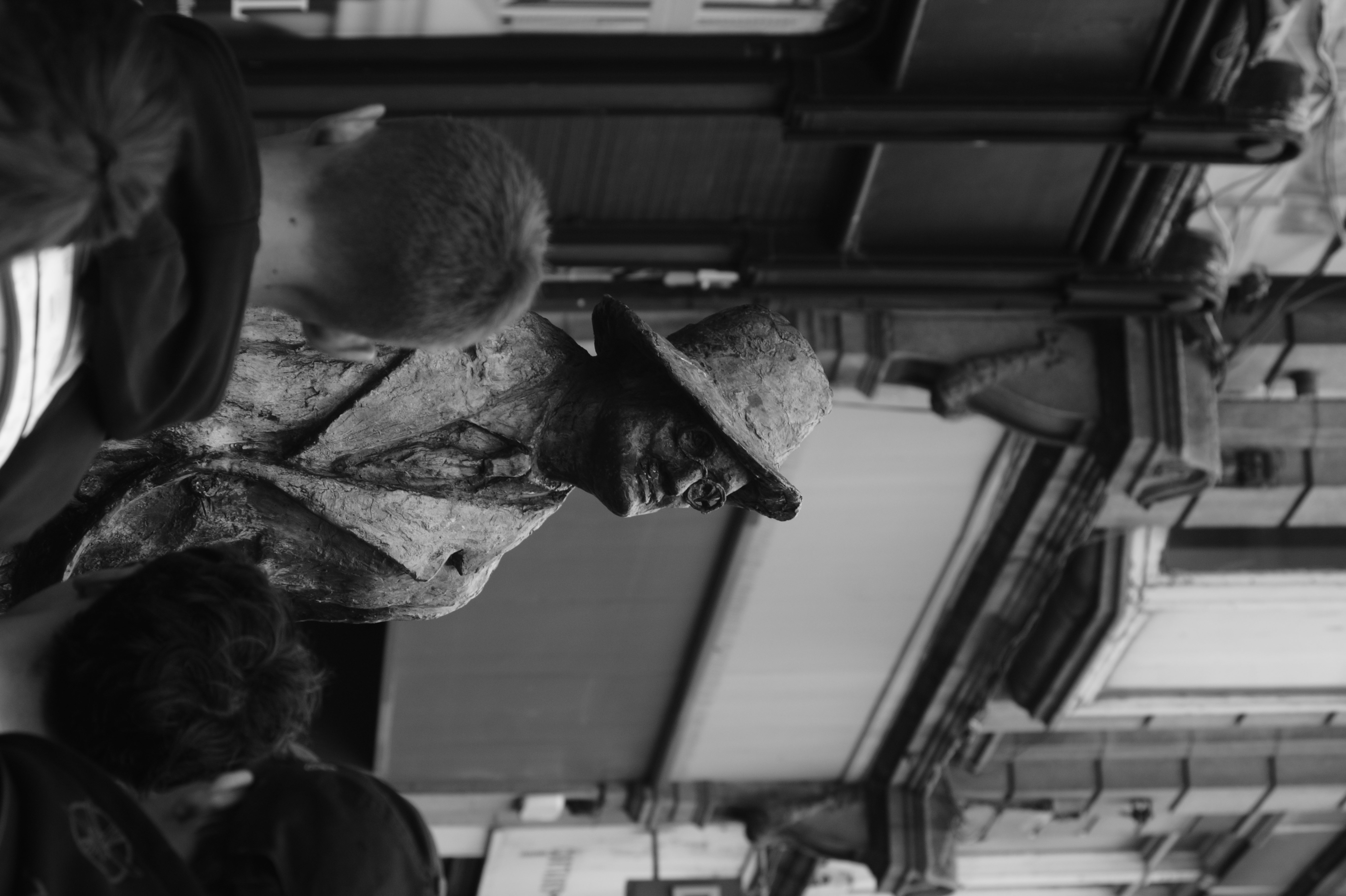 A passerby meets the gaze of a weathered street sculpture.