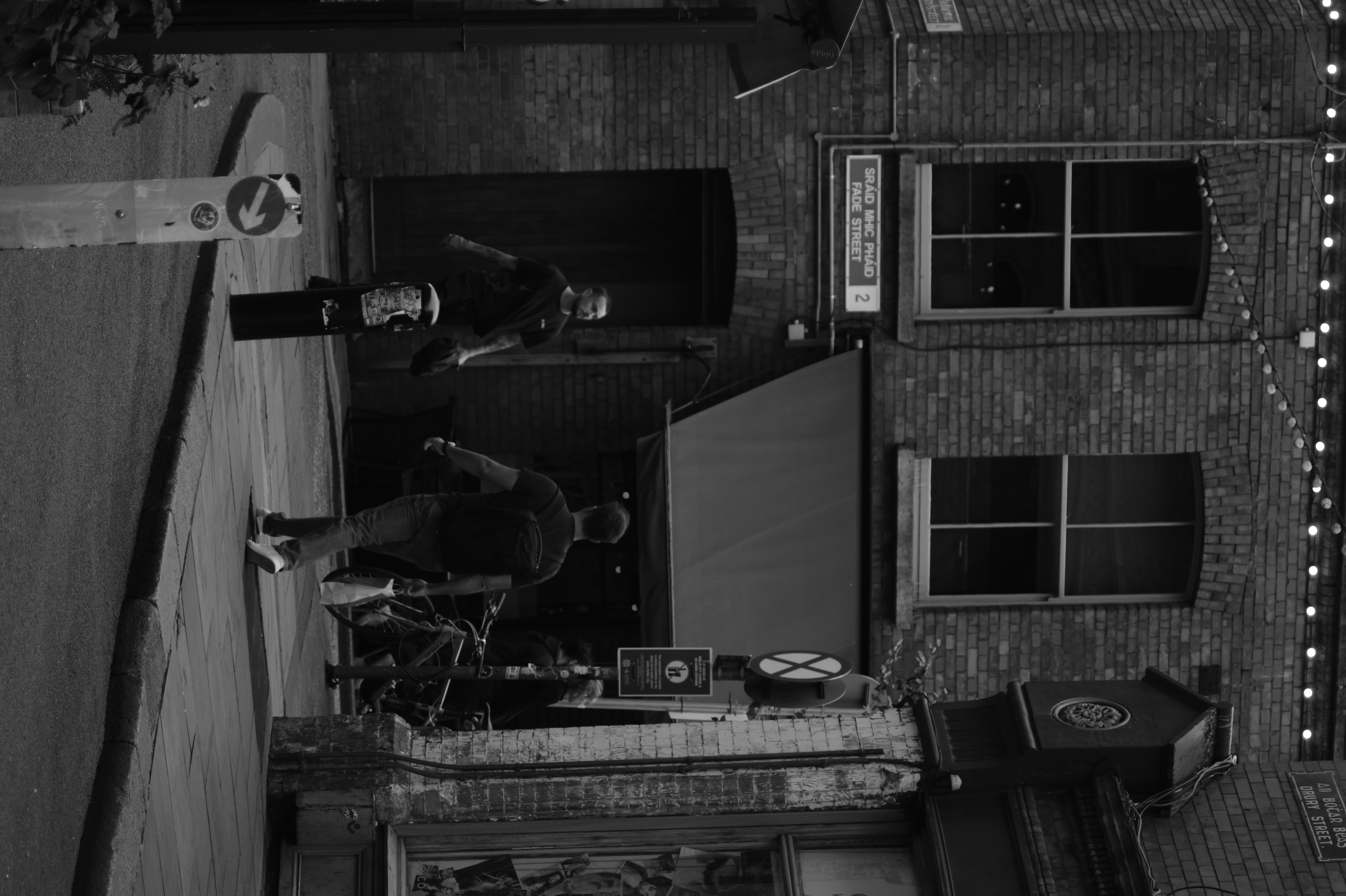 Two passersby cross paths in a narrow brick street.